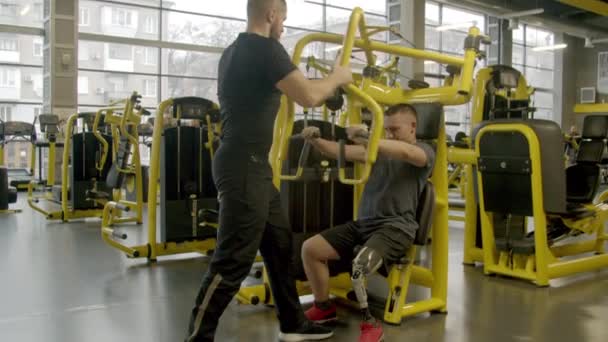 Niepełnosprawny młodzieniec z instruktorem ćwiczący na siłowni - Materiał filmowy, wideo