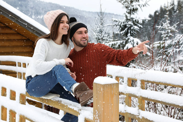 Happy couple near snowy wooden railing outdoors. Winter vacation - Photo, Image