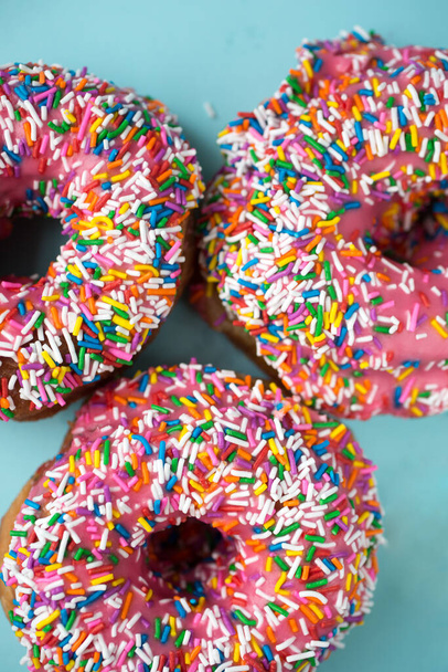 Three donuts with pink icing and candies on a blue pastel background - Photo, Image