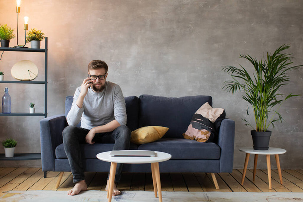 Young man in glasses angry talking on the phone sitting on the couch. Young businessman. - Photo, Image