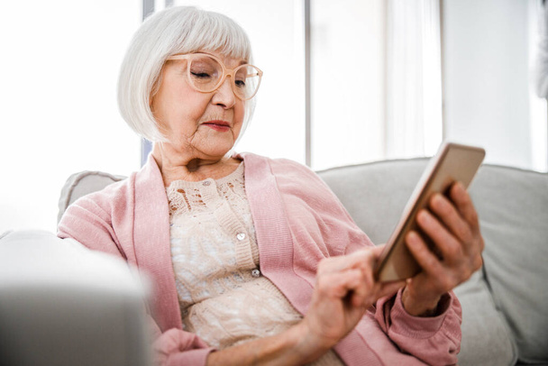 Senior lady using modern cellphone at home - Photo, Image
