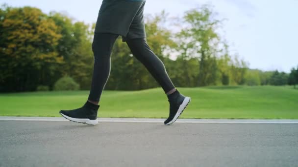 Spor ayakkabılı bir sporcu yolda koşuyor. Erkek bacakları dışarıda antrenman yapıyor. - Video, Çekim