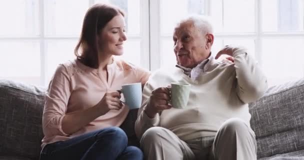 Happy grandfather and granddaughter talking drinking tea sit on sofa - Filmagem, Vídeo