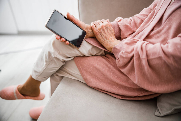 Öreg nő ül a kanapén és tartja a mobilját - Fotó, kép