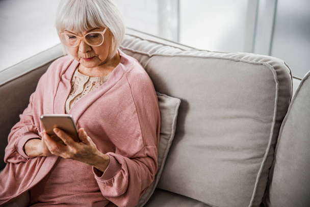 Senior woman sitting on sofa and using cellphone - Foto, immagini