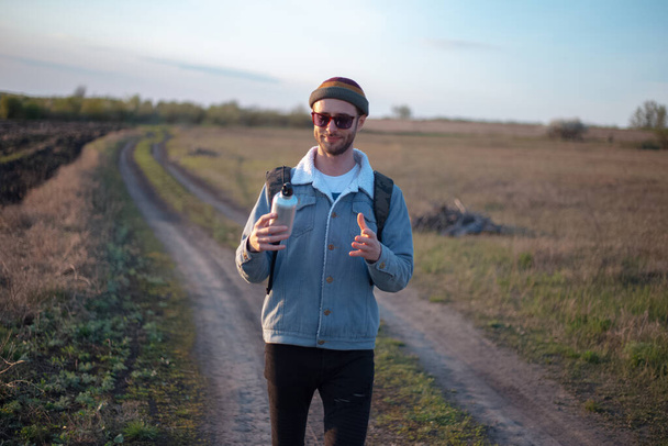 Retrato de hombre joven con mochila que sostiene la botella de agua termo de aluminio reutilizable en la mano
. - Foto, Imagen