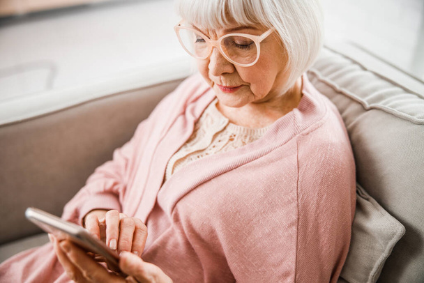 Elderly woman in glasses using modern smartphone - Фото, зображення