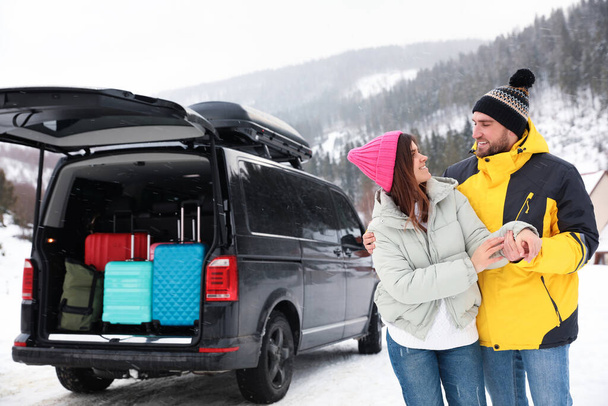 Happy couple near car with open trunk on snowy road. Winter vacation - Fotografie, Obrázek