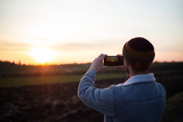 Vissza kilátás fiatal srác fotózni naplemente okostelefon. - Fotó, kép