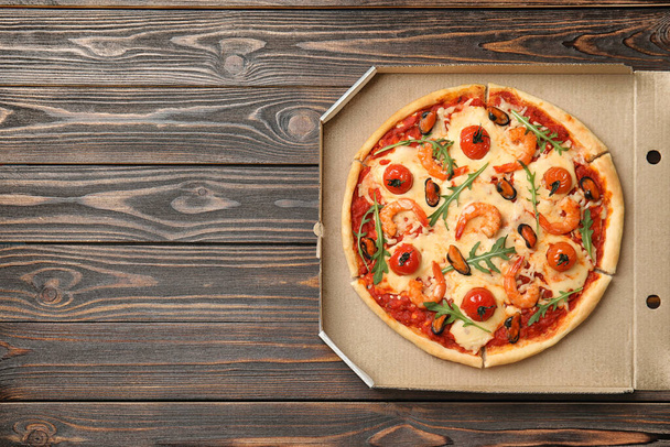 Вкусная пицца из морепродуктов в картонной коробке на деревянном столе, вид сверху. Пространство для текста
 - Фото, изображение