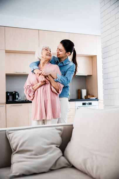 Happy grandmother and adult granddaughter hugging at home - Foto, afbeelding