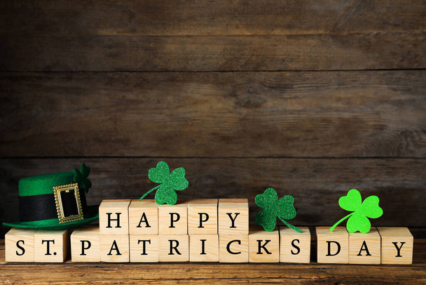 Wooden cubes with words HAPPY ST PATRICK'S DAY, green leprechaun hat and clover leaves on table - Foto, Imagen