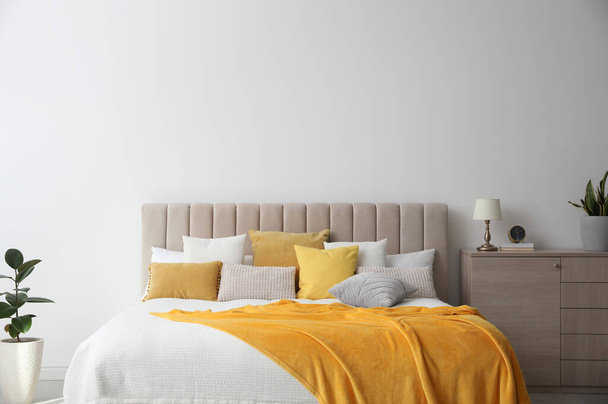 Stilvolles Schlafzimmer-Interieur mit weichen gelben Kissen und Decke - Foto, Bild