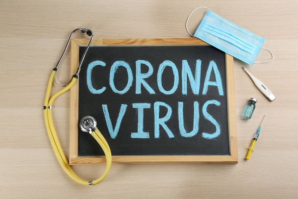 Chalkboard with words CORONA VIRUS and stethoscope on wooden background, flat lay - Foto, immagini
