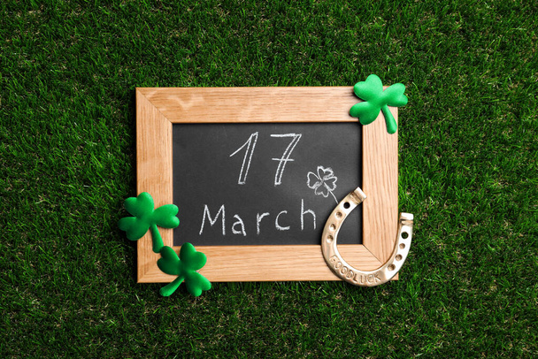 Flat lay composition with horseshoe and chalkboard on grass. St. Patrick's Day celebration - Fotó, kép