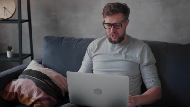 Young bearded man with glasses is working on a laptop. Freelance. - Кадры, видео