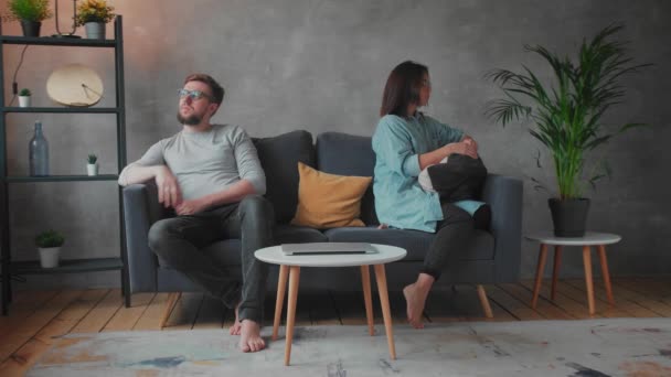 Ένα νεαρό ζευγάρι κάθεται στον καναπέ μετά από μια διαφωνία στο σπίτι. Ο σύζυγος και η σύζυγος κάθονται με τις τσάντες τους ο ένας στον άλλο. Κοινωνικό βίντεο. - Πλάνα, βίντεο