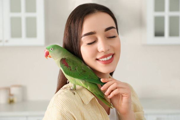 Young woman with Alexandrine parakeet indoors. Cute pet - Φωτογραφία, εικόνα