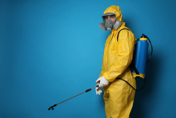 Man wearing protective suit with insecticide sprayer on blue background, space for text. Pest control - Zdjęcie, obraz