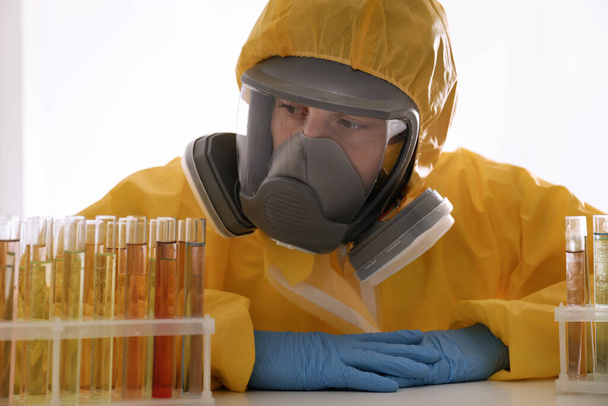Επιστήμονας με στολή χημικής προστασίας που εργάζεται με δοκιμαστικούς σωλήνες στο τραπέζι. Έρευνα ιών - Φωτογραφία, εικόνα