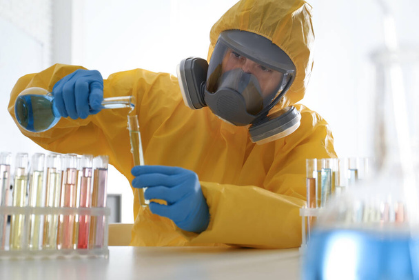 Scientist in chemical protective suit pouring reagent into test tube at laboratory. Virus research - Foto, imagen