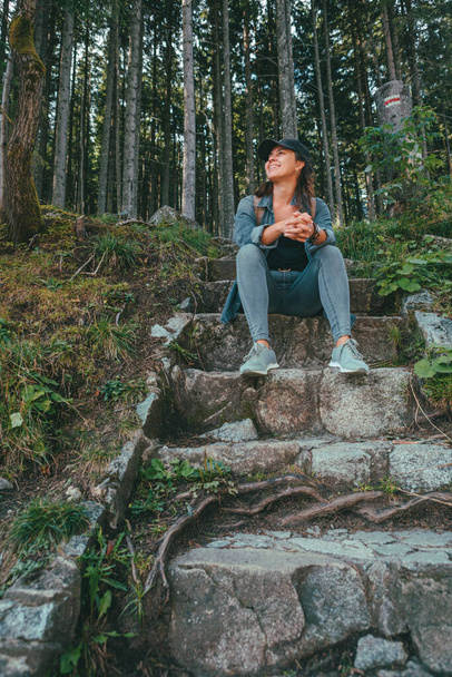 glimlachende vrouw wandelaar zittend aan stenen trap die leidt naar het bos - Foto, afbeelding
