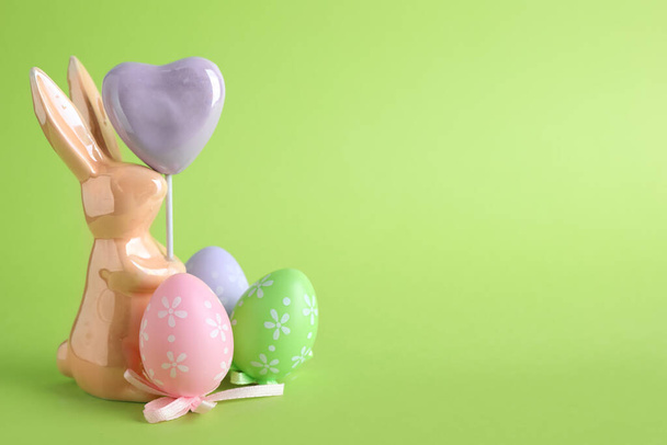 Easter bunny figure and dyed eggs on green background. Space for text - Фото, изображение