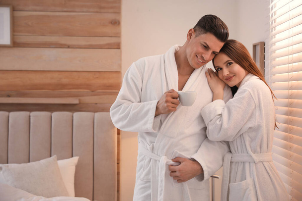 Happy couple wearing bathrobes near window in bedroom - Foto, Imagen