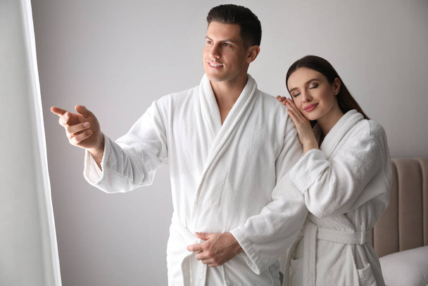 Happy couple wearing bathrobes near window in room - Photo, image