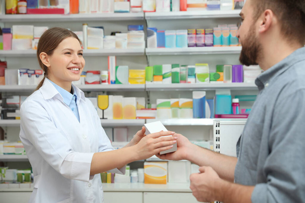Professional pharmacist giving medicine to customer in modern drugstore - Foto, Imagem