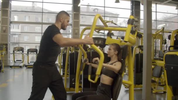 Jeune femme avec instructeur utilisant une presse thoracique dans la salle de gym
 - Séquence, vidéo