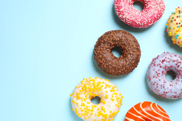 Delicious glazed donuts on light blue background, flat lay. Space for text - Zdjęcie, obraz