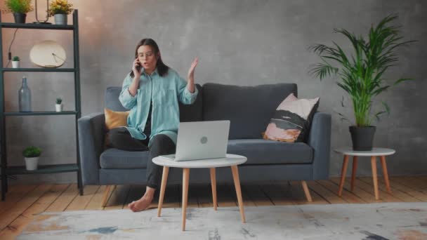Young Woman in glasses angry talking on the phone sitting on the couch. Young businesswoman. - Metraje, vídeo