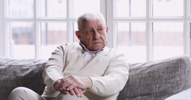 Pensive lonely older grandfather sitting alone on couch looking away - Metraje, vídeo
