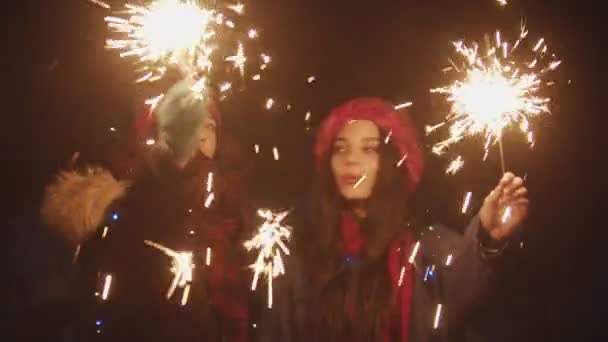 Two young smiling women playing with sparklers at night and looking in the camera - Záběry, video