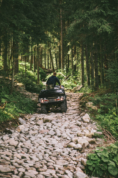 man on all-terrain vehicle ride by stone trail in forest summer time - Photo, Image