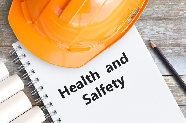 Sicherheit und Gesundheit mit orangefarbenem Helm, Bleistift und Notizbüchern auf Holztisch am Büroarbeitsplatz. - Foto, Bild