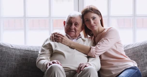 Happy young granddaughter embracing old grandfather sit on sofa, portrait - Imágenes, Vídeo