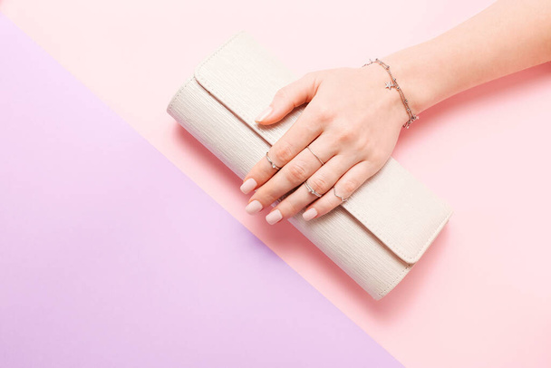 Female hand with jewelry and clutch bag on pink and lilac background - Fotografie, Obrázek