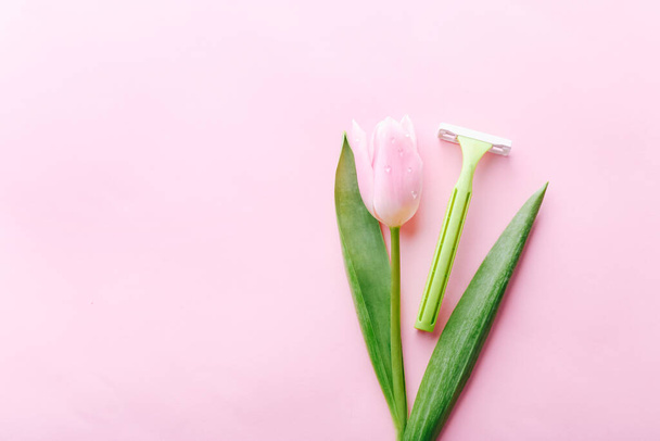 Green razor with beautiful pink tulip on a pink background. Hair removal concept. - Φωτογραφία, εικόνα