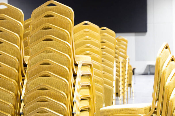 Stack Steel Chair Fabric seat pad yellow gold color and Table arrange in row ready to set up for big meeting, conference, business, workshop, gala dinner, Wedding ceremony in Convention Hall of Hotel - Photo, Image
