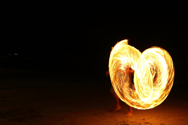 High Skill Man παίζοντας πυροτεχνήματα γυρίζοντας ξύλινο κοντάρι με πετρέλαιο και φωτιά, κύκλο γύρω ως δαχτυλίδι της φωτιάς στην παραλία κατά μήκος του ωκεανού στο τροπικό νησί, μεγάλη κίνηση θόλωμα έκθεση - Φωτογραφία, εικόνα