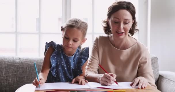 Older grandmother teaching preschool granddaughter drawing pencils together - Filmati, video