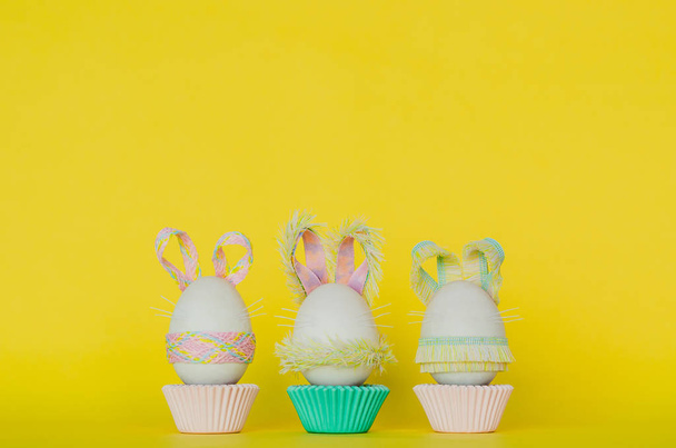 Huevos de Pascua decorar como aderezo de conejo poner en taza de papel magdalena colorido con fondo amarillo. Lindo concepto de foto creativa
. - Foto, Imagen