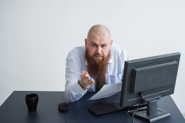 Porträt eines glatzköpfigen Mannes an einem Schreibtisch, der einen Bericht betrachtet und flucht. Der unzufriedene Chef berichtet dem Untergebenen. - Foto, Bild