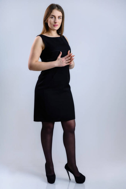Vertical portrait On a white background of a pretty smiling young Caucasian woman listens attentively in a black dress - Photo, Image