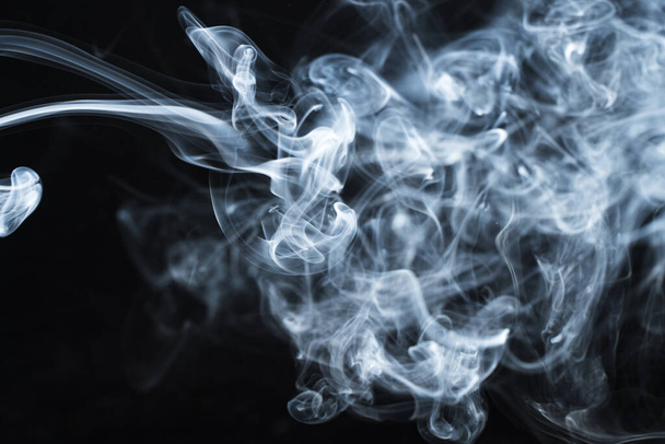 Background image of a wisp of smoke on a dark background. The texture of the flowing smoke. Frozen smoke on a dark background. Graphic resources dark backdrop. Texura of white clouds of fog. Curls of smoke frozen in motion. - Photo, Image