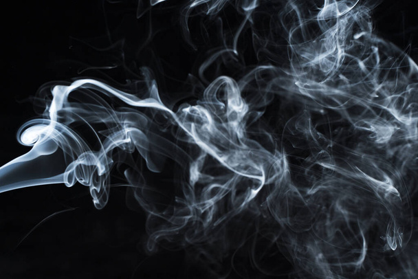 Background image of a wisp of smoke on a dark background. The texture of the flowing smoke. Frozen smoke on a dark background. Graphic resources dark backdrop. Texura of white clouds of fog. Curls of smoke frozen in motion. - Foto, Imagem