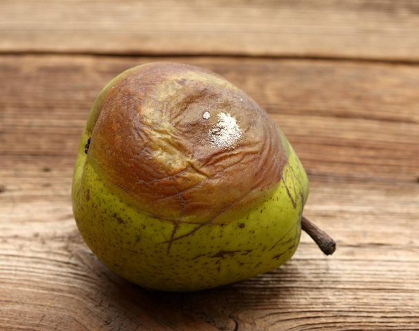 Verrotte peer op de tafel. beschimmeld perenfruit op een houten ondergrond - Foto, afbeelding