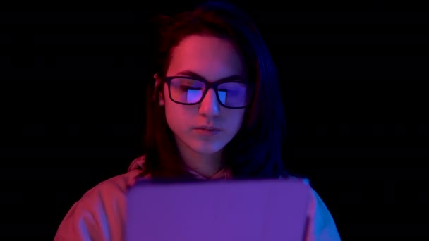 Mujer joven con una tableta. Una mujer está usando una tableta. Luz azul y roja cae sobre una mujer sobre un fondo negro
. - Imágenes, Vídeo